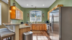 A kitchen with wooden cabinets, a stainless steel refrigerator, granite countertops, and a window with blinds. - Large Family Alert-Walk-In Lakeview-Sleeps 9-Pools-Near Silver Dollar City (Branson)