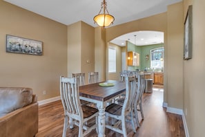 A dining area with a wooden table and white-painted chairs, a chandelier, and a painting on the wall.