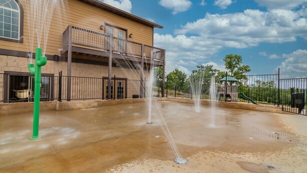 A water feature with multiple fountains in a courtyard, a building with a balcony, and a playground with slides in the background. - Large Family Alert-Walk-In Lakeview-Sleeps 9-Pools-Near Silver Dollar City (Branson)
