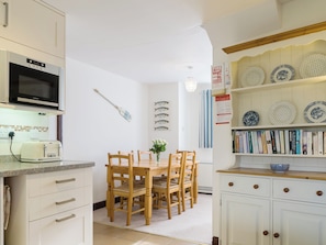 A kitchen with a microwave, toaster, wooden chairs, a dining table, and a bookshelf with books and decorative plates.