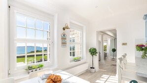 A bright, spacious kitchen with large windows, a dining area with a table set for breakfast, and a view of the sea. - Comfort Hill - Luxury, hot tub, sea views (Weymouth)