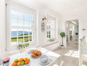 A bright, spacious kitchen with large windows, a dining area with a table set for breakfast, and a view of the sea. - Comfort Hill - Luxury, hot tub, sea views (Weymouth)