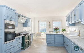 A modern kitchen with light blue cabinets, a central island, and a dining area with white chairs. - Comfort Hill - Luxury, hot tub, sea views (Weymouth)