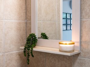 A bathroom with a mirror, a shelf with a candle, and a green plant. - Riverwalk Apartment One (Slough)