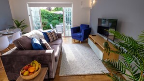 En moderne stue med sofa, lænestole, et fjernsyn og et spiseområde med bord og stole.