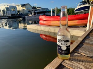 A Corona Extra beer bottle on a wooden dock with a calm body of water and boats in the background.