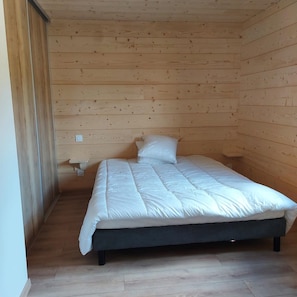 Quarto pequeno com uma cama de solteiro, paredes de madeira e uma cama simples.