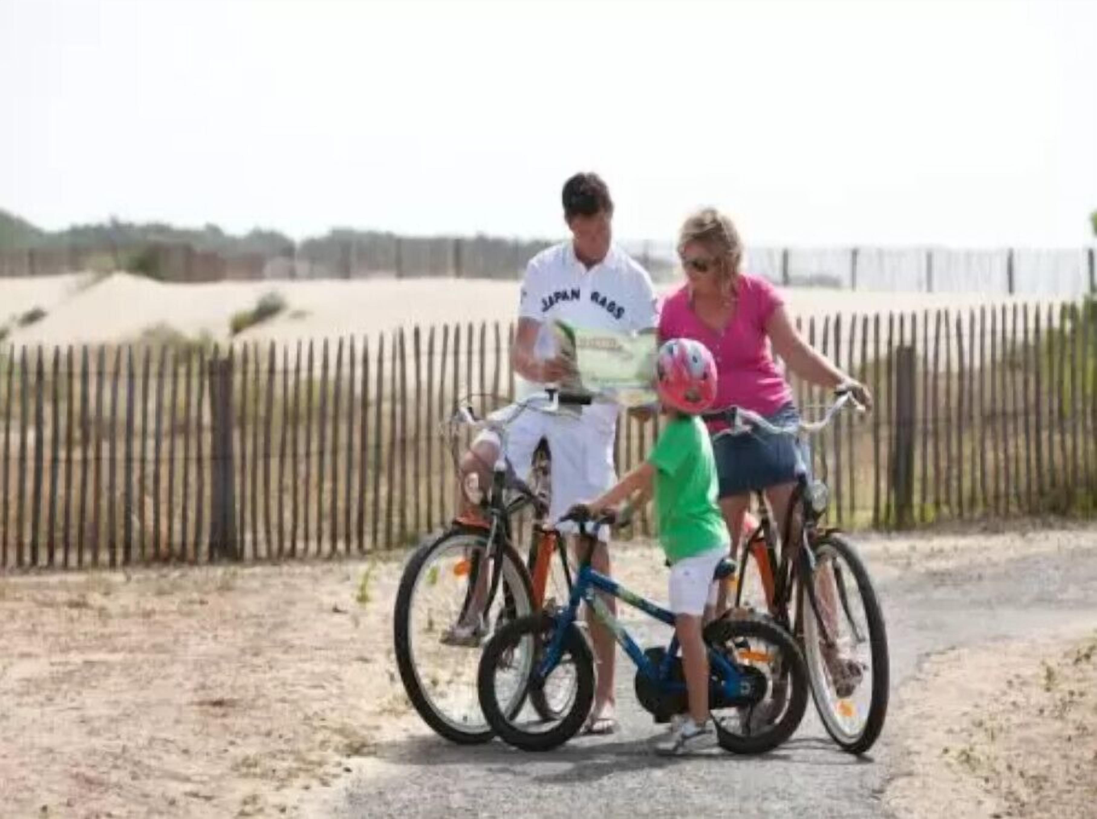 A family with two bicycles on a dirt path with a wooden fence in the background.