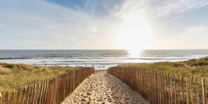 A sandy beach path leading to the ocean with wooden fences on either side.