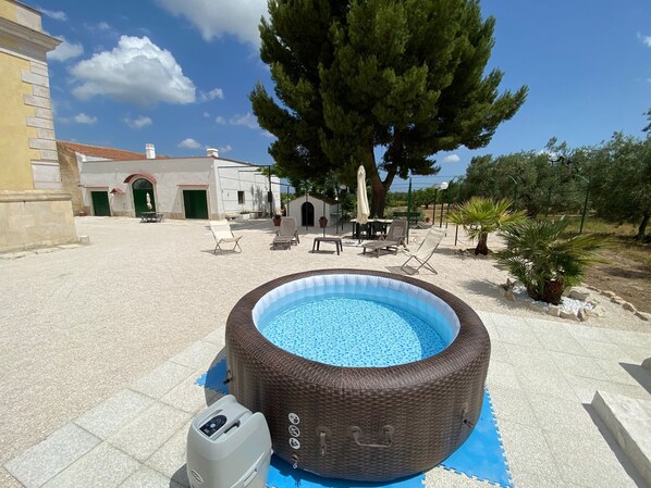An outdoor swimming pool with lounge chairs and a pergola, surrounded by a landscaped garden and a building with a tiled roof.