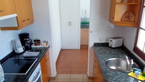 A kitchen with a stove, oven, coffee maker, and a toaster. There is a sink and a window with a view of the outside.