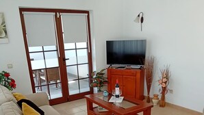 A living room with two sofas, a coffee table, a TV, and a sliding glass door leading to an outdoor area.