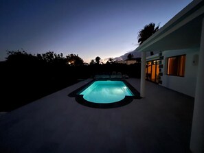 A swimming pool with a light blue water feature, surrounded by a concrete deck and a modern house with large windows. - Welcome to Villa Jaxx (Playa Blanca)