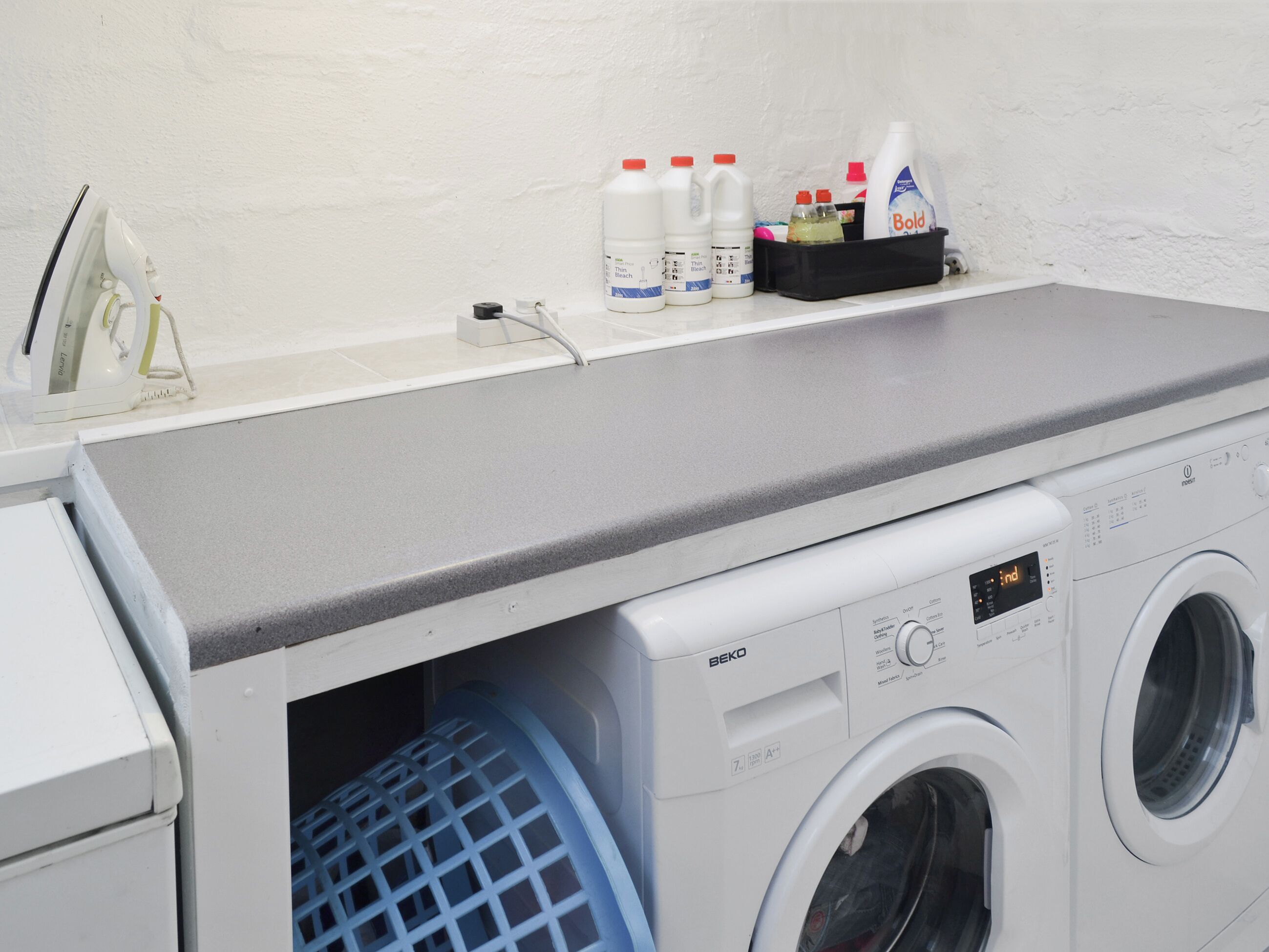 A front-loading washing machine with a control panel, a drying rack, and a shelf with cleaning supplies.