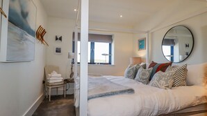 Une chambre spacieuse avec un grand lit, une chaise avec des serviettes, une table de chevet et une fenêtre donnant sur un beau paysage.