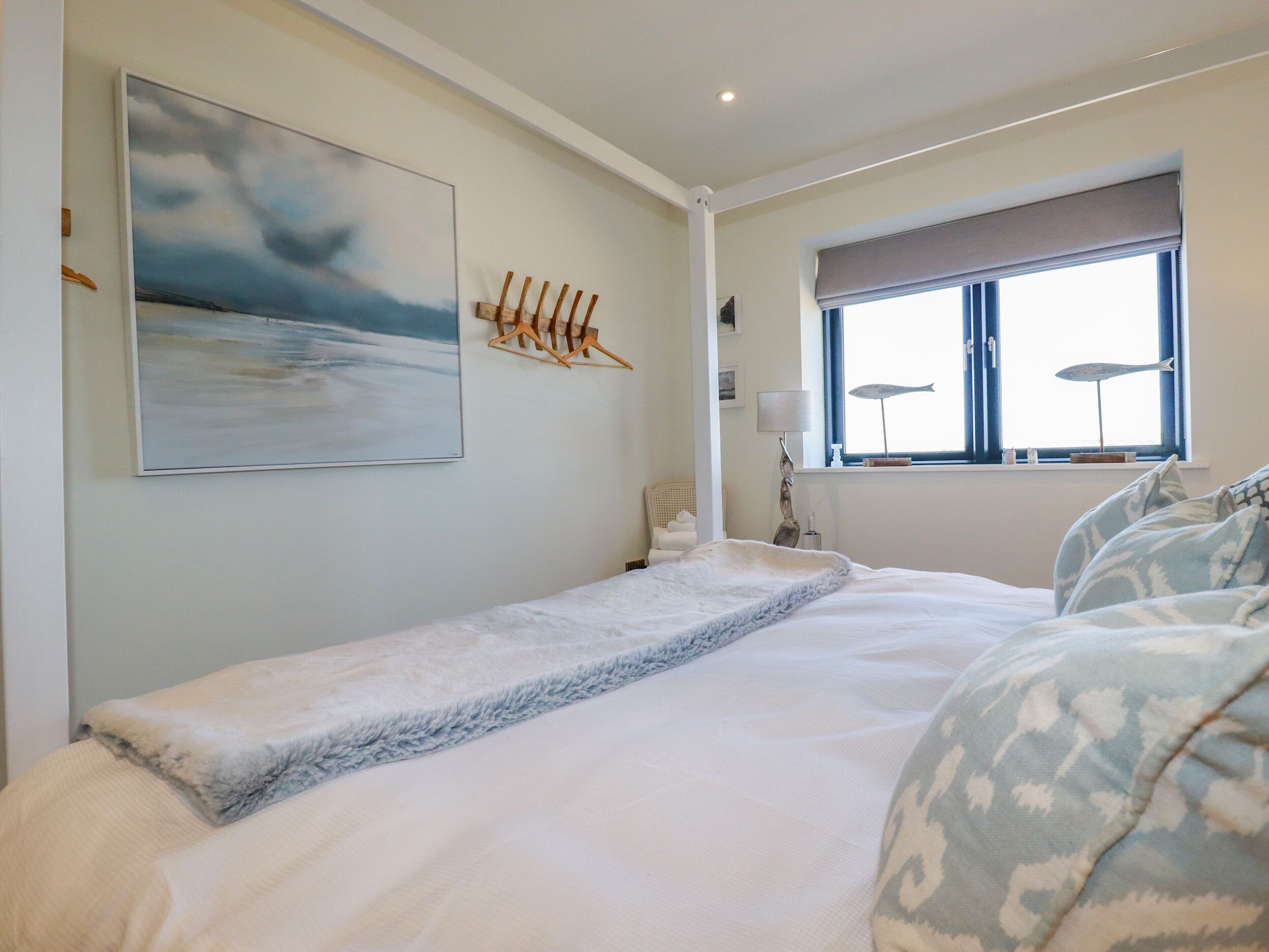 Une chambre à coucher avec un lit, une fenêtre avec des stores, une lampe fixée au mur et un tableau.