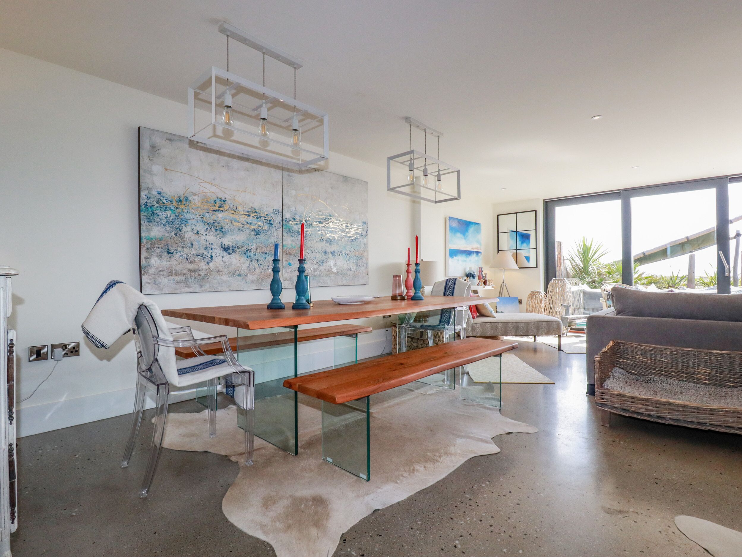 A modern living room with a wooden bench, glass tables, and a large abstract painting on the wall.
