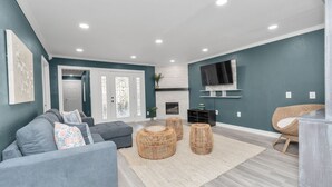 Un salon moderne avec un canapé gris, des poufs en osier et un téléviseur à écran plat fixé au mur.