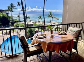 Un balcon avec une table et des chaises en verre, donnant sur une piscine et offrant une vue sur l’océan.