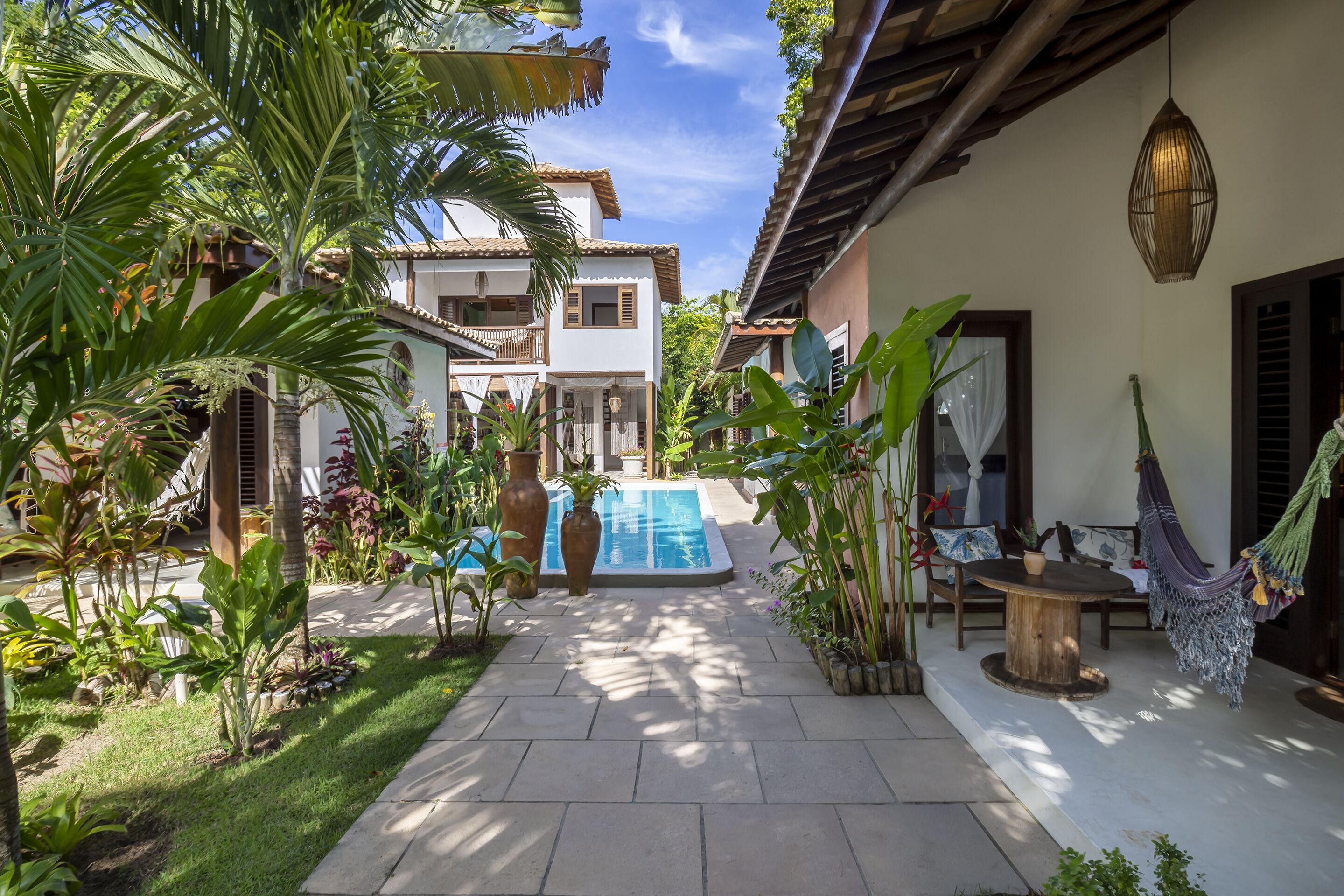 Un patio con piscina, rodeado de abundante vegetación y una hamaca.