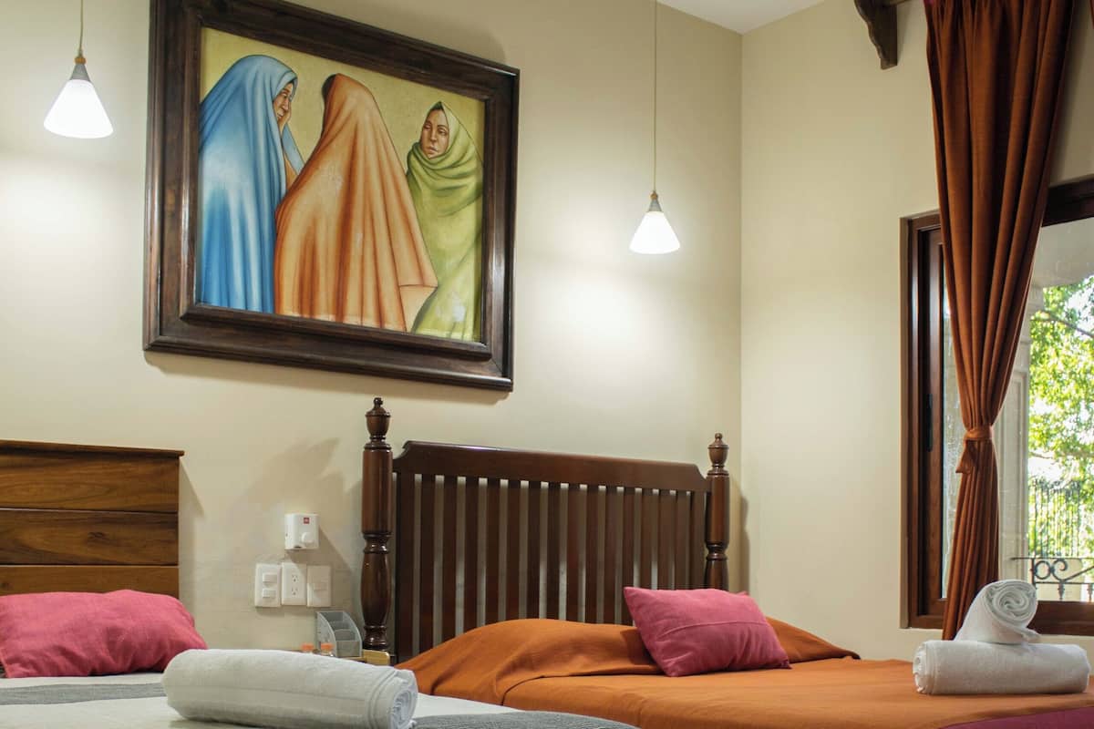 Ein Hotelzimmer mit zwei Betten, einem Deckenventilator, einem Bild an der Wand und einem Fenster mit Vorhängen.