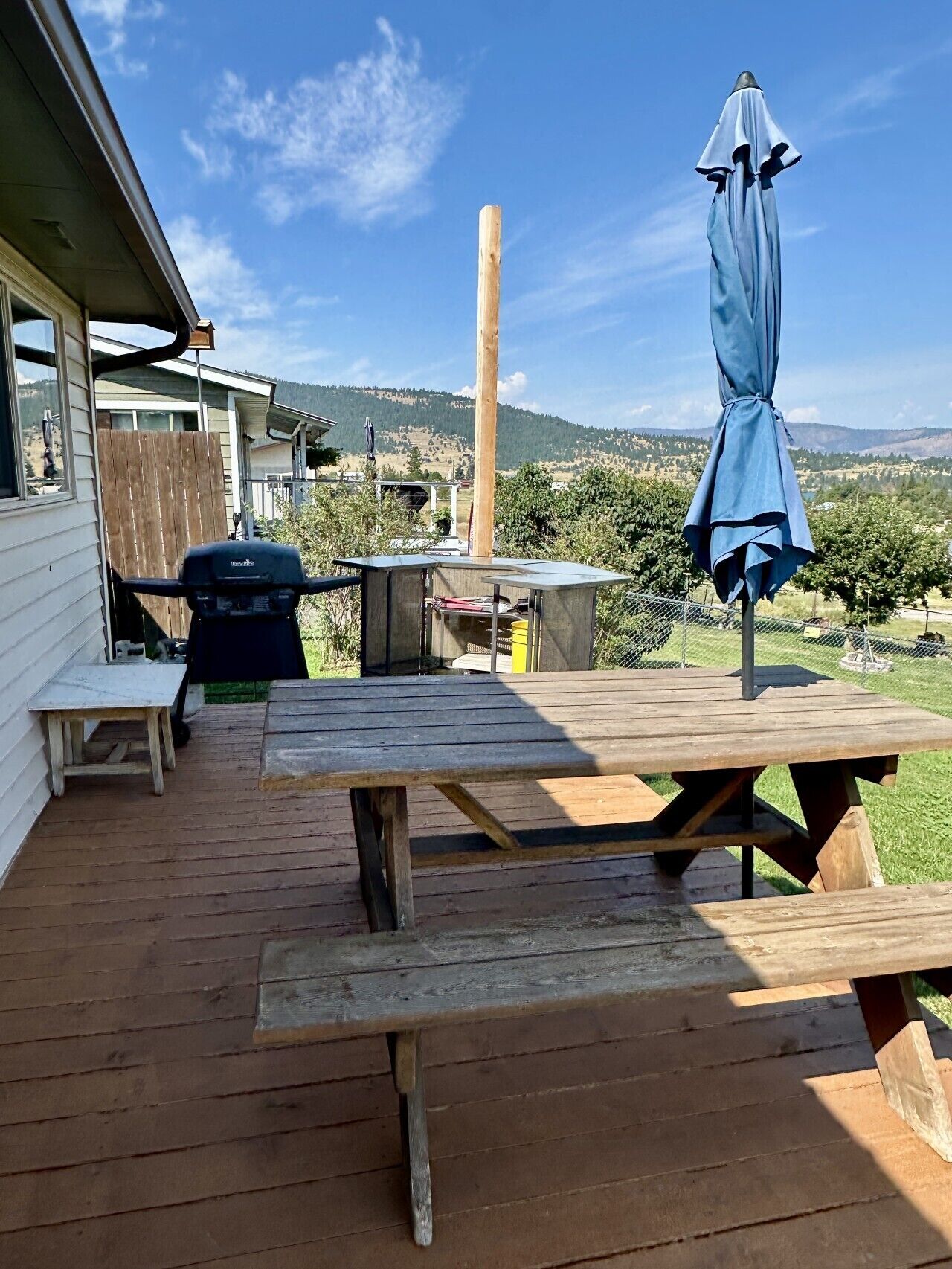 A wooden deck with picnic tables and a barbecue grill, overlooking a hilly landscape.