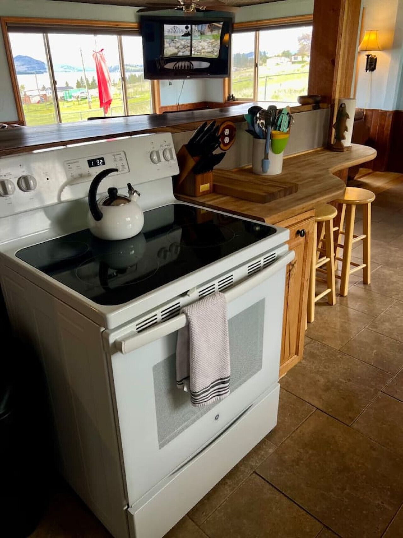 A kitchen with a stove, a kettle, a wooden countertop, and a window with a view of the outdoors.