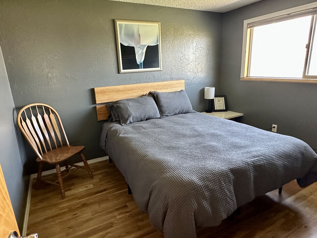 Una camera da letto con un letto di legno, una sedia, un comodino e una finestra.
