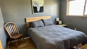 Une chambre à coucher avec un lit en bois, une chaise, une table de chevet et une fenêtre.