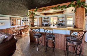 Una cocina con barra de madera, taburetes de bar, una mesa de comedor con sillas y una planta en maceta.