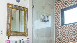 Ein Badezimmer mit einem Holzkosmetikschrank, einem großen Spiegel und einer Dusche mit gemusterten Fliesen.