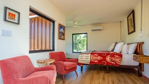 Ein Schlafzimmer mit einem Bett, zwei roten Sessel, einem kleinen runden Tisch und einem Fenster mit Jalousien.