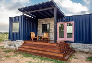Et moderne modulhus med en stenvæg, en overdækket veranda og en pink dør.