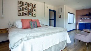 Een slaapkamer met een groot bed, een bureau en een stoel. Een deur leidt naar de badkamer en er is een raam met jaloezieën.