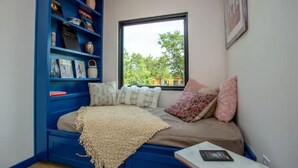 Een slaapkamer met een bed, een raam, een boekenkast en uitzicht op bomen en gebouwen.