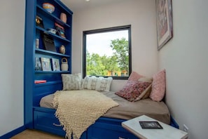 Cozy bedroom with a bookshelf, comfortable bed, and a window offering a view of the surrounding greenery.