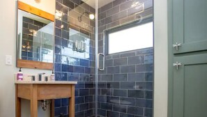 A bathroom with dark blue tiled walls, a wooden vanity, a glass shower enclosure, and a green door. - Tranquility at Odonata Escape --- Chic modern container home in a country setting (Fredericksburg)