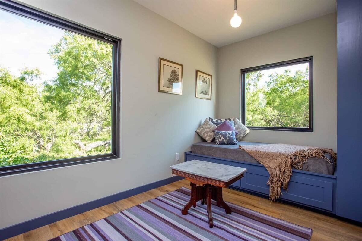 Una habitación con ventanas amplias, un banco con cojines y una pequeña mesa.