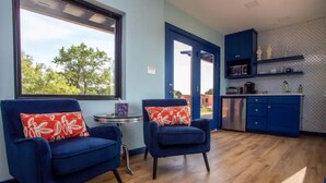 Ein Zimmer mit zwei blauen Sesseln, einem kleinen runden Tisch und Blick ins Freie durch ein Fenster.