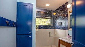 Ein Badezimmer mit blauer Tür, einer Duschkabine aus Glas und einem weißen Waschbecken mit Holzunterschrank.