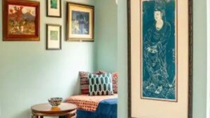 Ein Zimmer mit einem Bett, einem runden Tisch mit einer Schüssel und gerahmten Kunstwerken an der Wand.