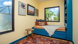 Ein Schlafzimmer mit einem Bett, einem kleinen Tisch, einem Fenster und einer Wand mit gerahmten Bildern.