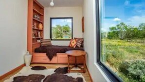 Ein gemütliches Zimmer mit großem Fenster, einer Couch, einem kleinen Tisch und einem Bücherregal.
