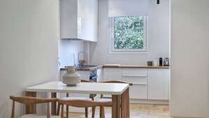 A modern kitchen with white cabinets, a wooden countertop, and a window with a view of greenery. There is a table with chairs and a vase on it. - Sleeping with the Ancient Gods in Koukaki (Athina)