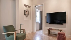 A modern living room with a green armchair, a flat-screen TV mounted on the wall, a small wooden table with books, and a pink ottoman. - Sleeping with the Ancient Gods in Koukaki (Athina)