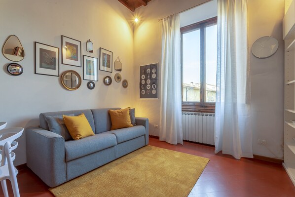 A living room with a sofa, a coffee table, a radiator, and a window with curtains. - Discover Florence and feel right at home (Firenze)