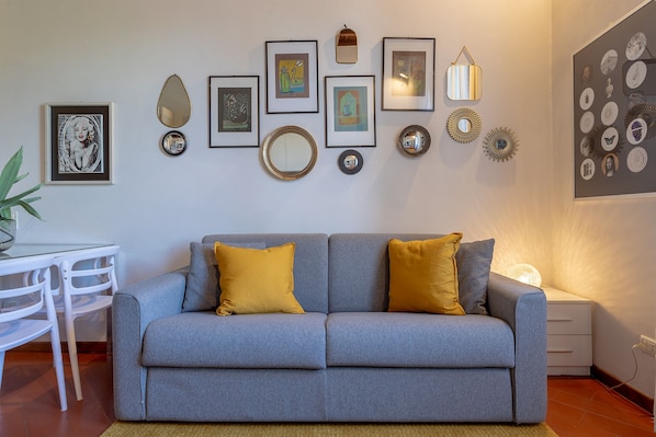 A modern living room with a grey sofa, two mustard-colored cushions, and a dining area with a white table and chairs.