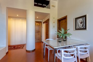 A dining area with a glass table, white chairs, a potted plant, and wooden doors.