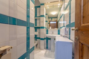 A bathroom with white and teal tiles, a sink, a mirror, and a wooden door. - Discover Florence and feel right at home (Firenze)