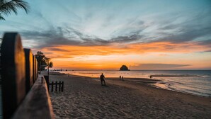 Una playa con una valla de madera, gente caminando y un atardecer.
